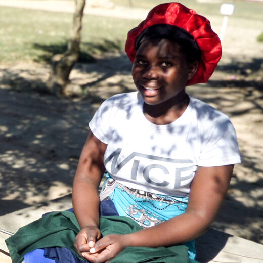 A young Zimbabwean woman smiles at the camera, the clothes she has made on her lap
