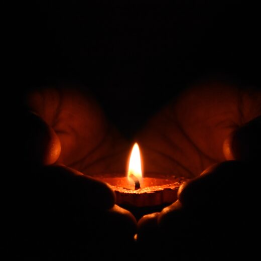 A candle burning in cupped hands