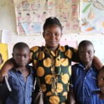 Penlope, our partner in Rukungiri Uganda, with her arms round some school children, all smiling to the camera.