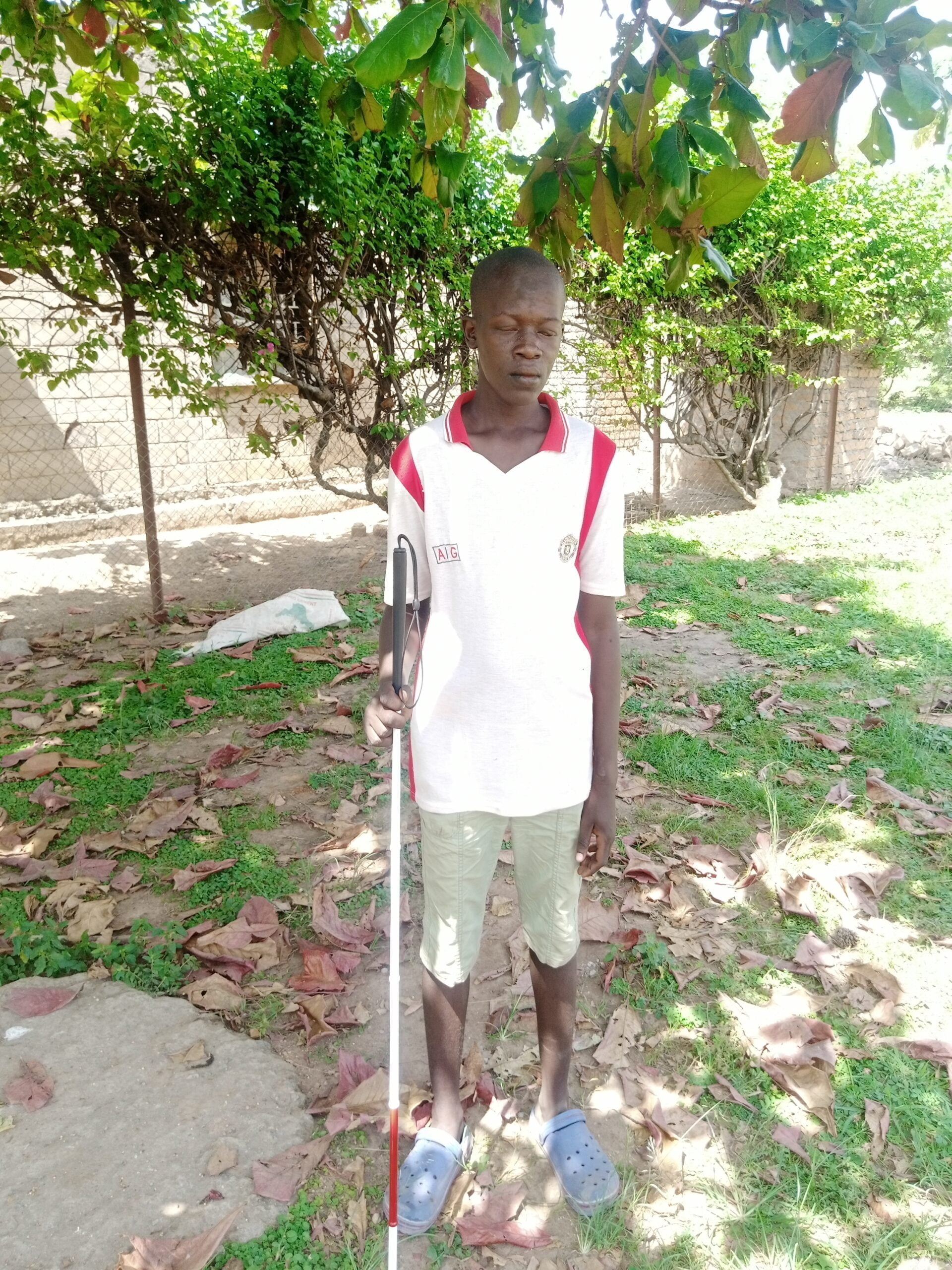 Nelson stands under a tree in a white t-shirt. He's carrying his white cane.